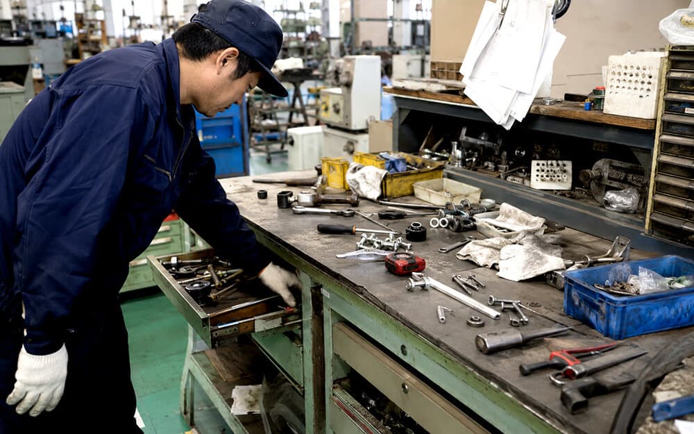 工具や小物部品が散らかった作業台で工具を探す現場担当者
