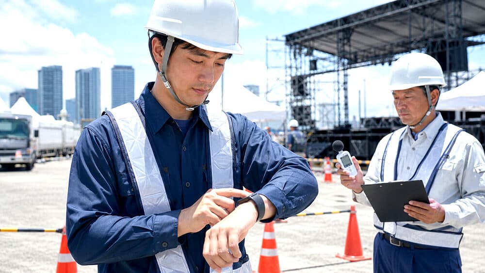 屋外作業員が腕時計型の熱中症アラートを確認するイメージ