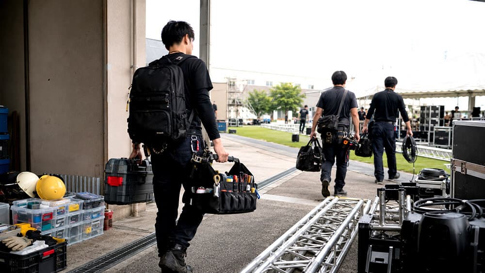屋外現場やイベント設営で工具バッグを持ち運ぶ作業員